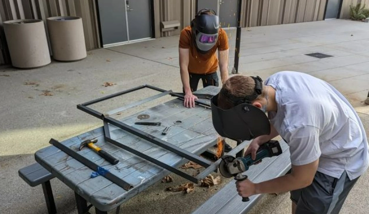 Photo of Felipe grinding down unnecessary welds while Jacob holds the frame stable.