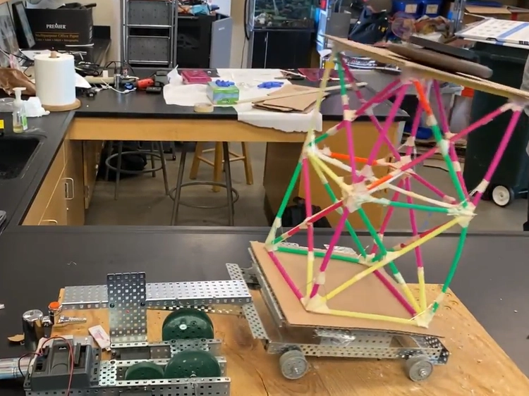 Photo of small table-top machine shaking a straw tower built on top of it.